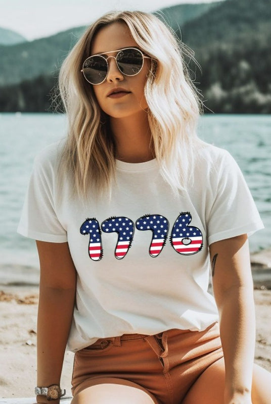 Close-up image of a USA July 4th graphic tee with the number '1776' spelled out in American flag inspired numbers on the front. This patriotic tee is perfect for celebrating Independence Day in style and showing off your love for America on a white graphic tee. 