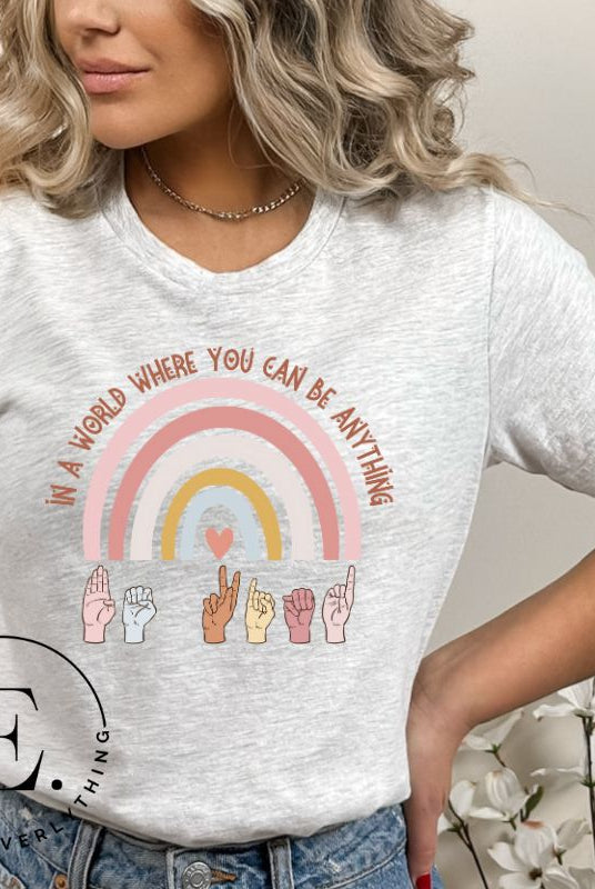 American sign language shirt with a rainbow and the phrase "In a world where you can be anything" and hands signing 'Be Kind' at the bottom on the rainbow on a grey colored shirt.
