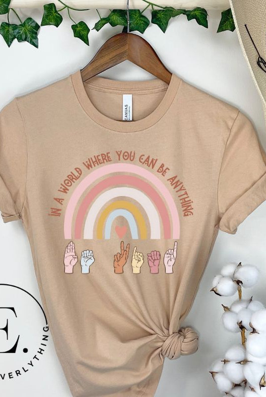 American sign language shirt with a rainbow and the phrase "In a world where you can be anything" and hands signing 'Be Kind' at the bottom on the rainbow on a tan colored shirt.