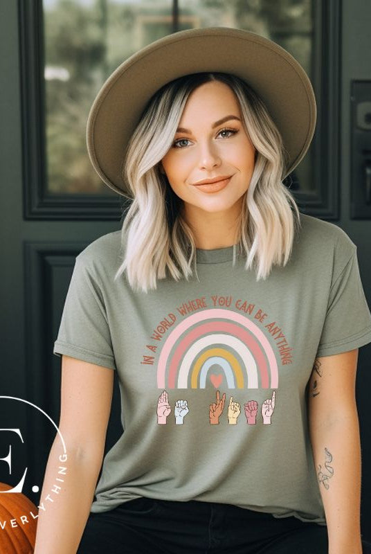 American sign language shirt with a rainbow and the phrase "In a world where you can be anything" and hands signing 'Be Kind' at the bottom on the rainbow on a green colored shirt.
