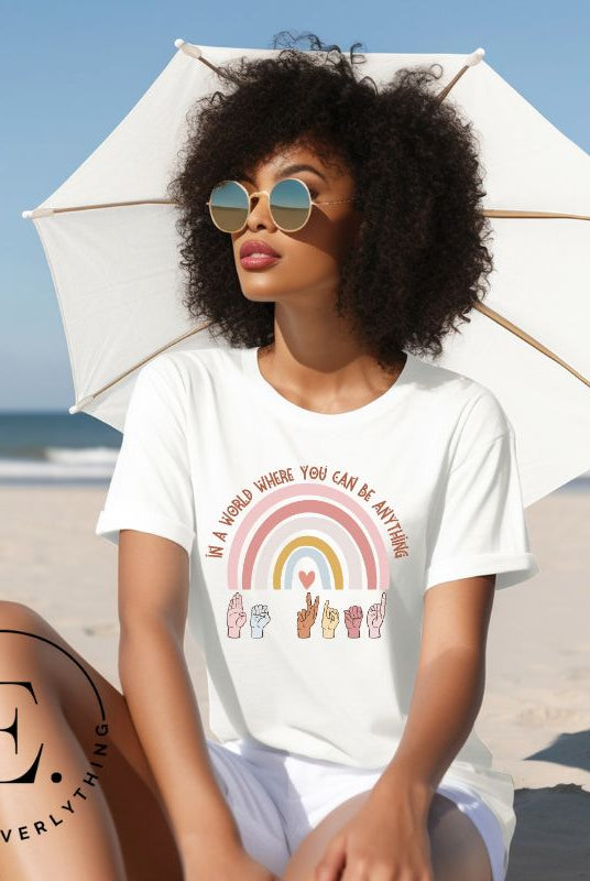 American sign language shirt with a rainbow and the phrase "In a world where you can be anything" and hands signing 'Be Kind' at the bottom on the rainbow on a white colored shirt. 