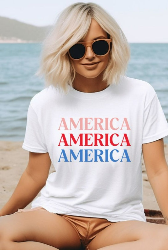 Close-up image of a USA July 4th graphic tee with the word 'America' repeated three times in bold lettering on the front. This festive tee is perfect for celebrating Independence Day in style and showing off your patriotic spirit on a white graphic tee. 