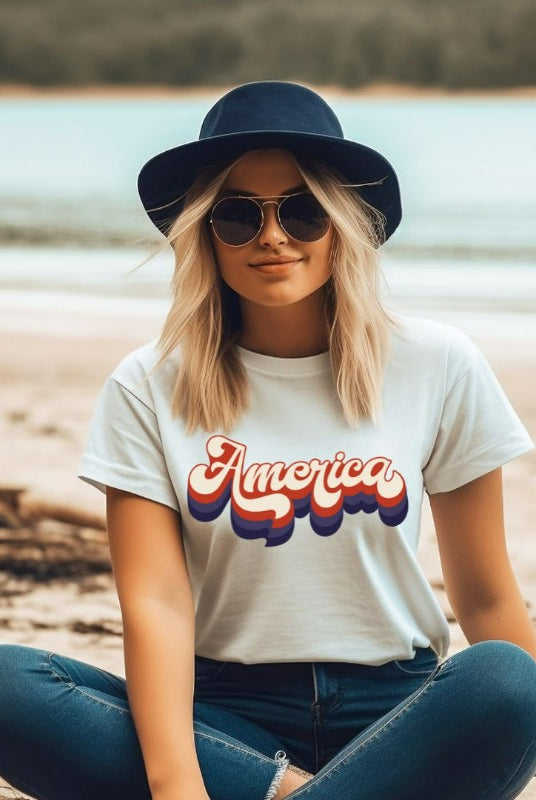 Close-up image of a USA July 4th graphic tee with the word 'America' spelled out in funky retro lettering on the front. This vintage-inspired tee is perfect for adding a fun and nostalgic touch to your Independence Day celebrations on awhite grapchi tee. 