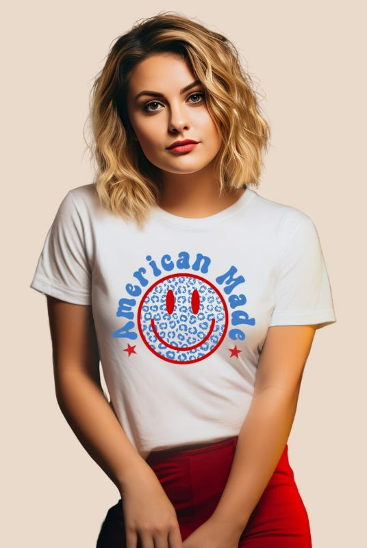Close-up image of a USA July 4th graphic tee featuring the words 'American Made' surrounded by retro lettering around a bold blue cheetah print retro smiley face on the front. A playful and unique design perfect for celebrating July 4th in style on a white graphic tee. 