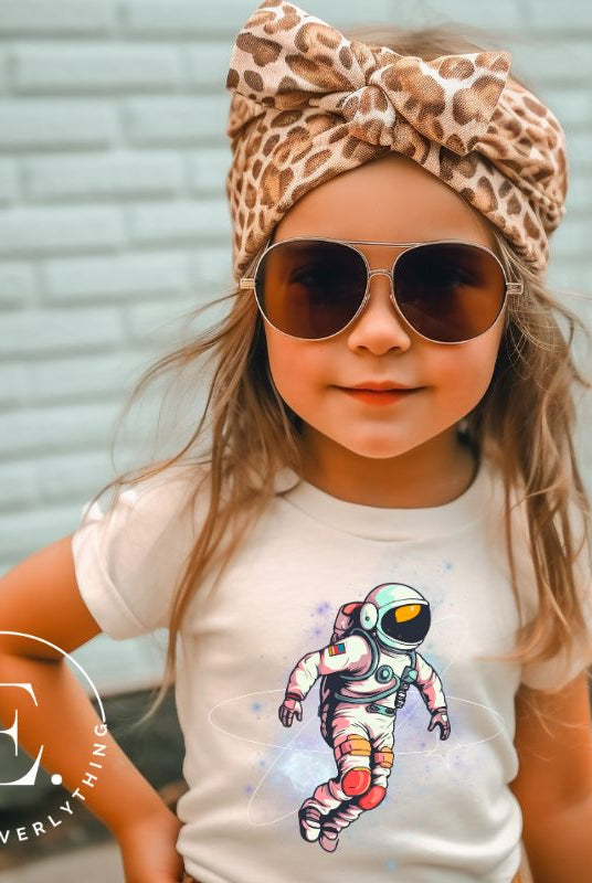 Embark on an intergalactic adventure with our captivating kids' shirt! Featuring a whimsical design of an astronaut floating in space on a soft cream shirt. 