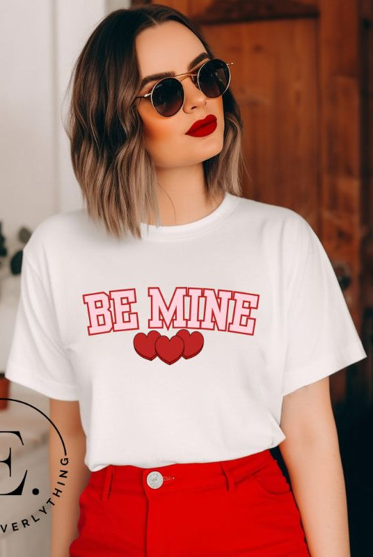 Elevate your Valentine's Day style with our "Be Mine" shirt! Featuring bold athletic lettering and three adorable hearts, on a white shirt. 
