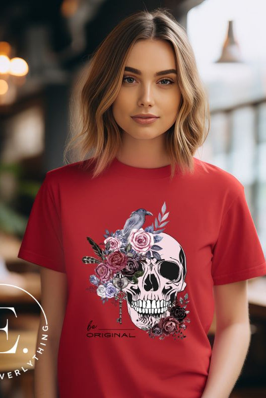 Looking for a unique Halloween shirt? Look no further! Our hauntingly beautiful shirt features a floral skull, raven, and the empowering slogan 'Be Original'. Stand out from the crowd with this unforgettable statement piece on a red shirt. 