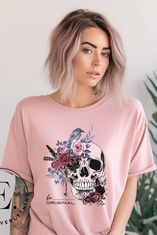 Looking for a unique Halloween shirt? Look no further! Our hauntingly beautiful shirt features a floral skull, raven, and the empowering slogan 'Be Original'. Stand out from the crowd with this unforgettable statement piece on a pink shirt. 