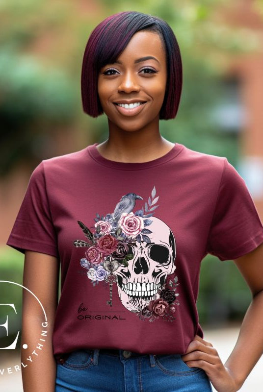 Looking for a unique Halloween shirt? Look no further! Our hauntingly beautiful shirt features a floral skull, raven, and the empowering slogan 'Be Original'. Stand out from the crowd with this unforgettable statement piece on a maroon shirt. 