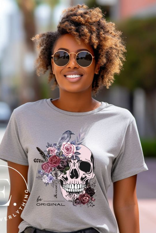 Looking for a unique Halloween shirt? Look no further! Our hauntingly beautiful shirt features a floral skull, raven, and the empowering slogan 'Be Original'. Stand out from the crowd with this unforgettable statement piece on a grey shirt. 
