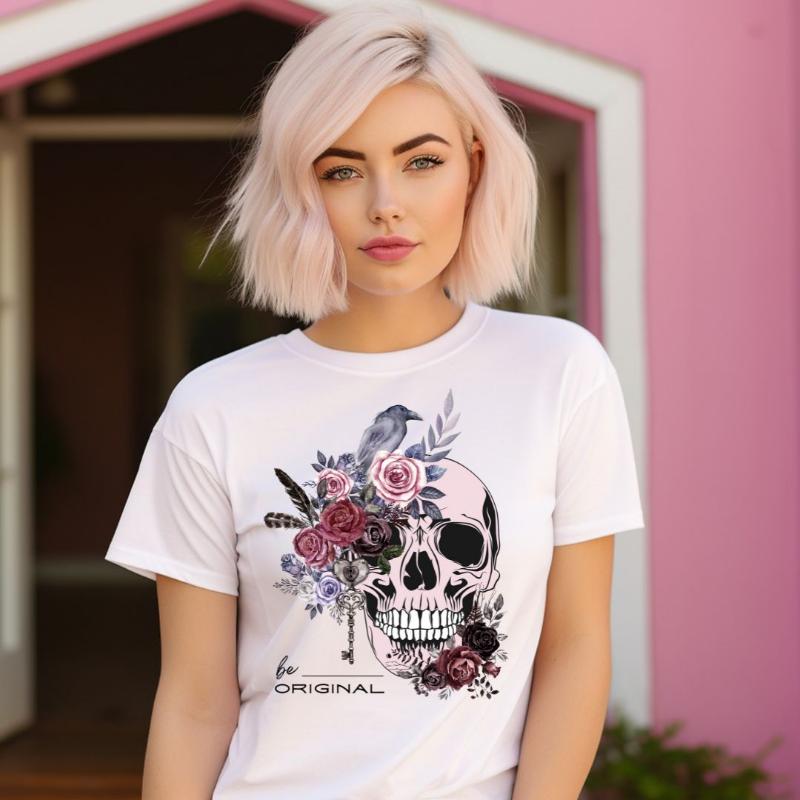 A Halloween-themed design with a skull adorned with flowers and a raven, accompanied by the text "Be Original." The shirt is soft and perfect for celebrating Halloween in style on a white shirt.