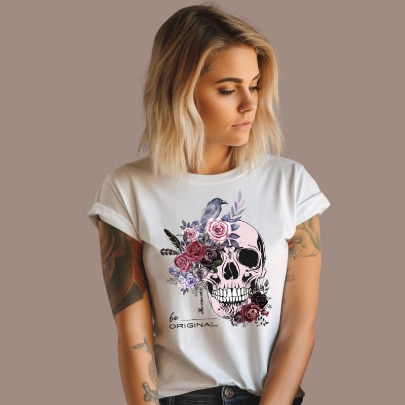 A Halloween-themed design with a skull adorned with flowers and a raven, accompanied by the text "Be Original." The shirt is soft and perfect for celebrating Halloween in style on a white shirt.