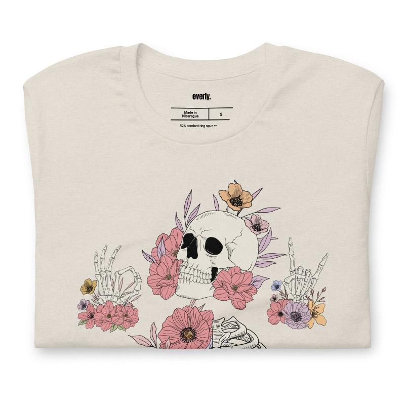 Heather dust t-shirt featuring a detailed skeleton design with ribcage and hands intertwined with soft, colorful flowers, blending gothic and floral aesthetics.