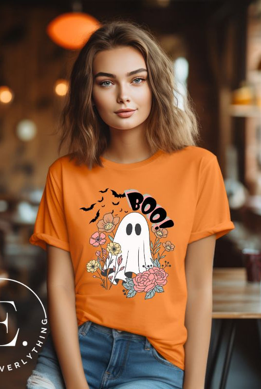 Get ready for Halloween with our cute and spooky ghost-themed shirt! Featuring a whimsical design with a cute ghost, flowers, and bats in a starry sky, it's the perfect blend of spooky and sweet on an orange shirt. 