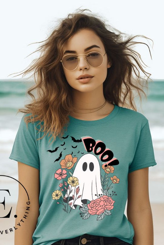 Get ready for Halloween with our cute and spooky ghost-themed shirt! Featuring a whimsical design with a cute ghost, flowers, and bats in a starry sky, it's the perfect blend of spooky and sweet on a teal shirt. 