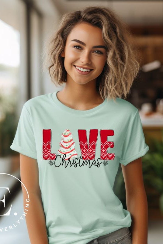 Spread love and joy this holiday season with our Christmas shirt featuring the classic Christmas tree cake, which is incorporated into the word "Love" on a mint colored shirt. 