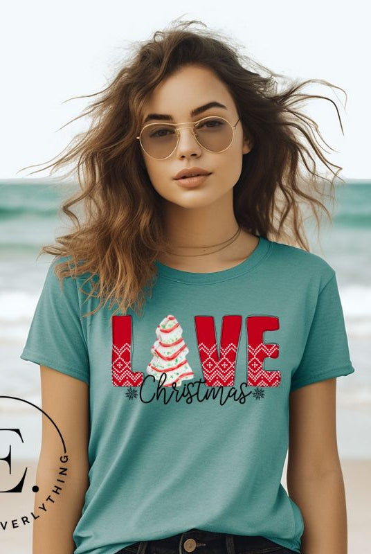 Spread love and joy this holiday season with our Christmas shirt featuring the classic Christmas tree cake, which is incorporated into the word "Love" on a teal colored shirt.