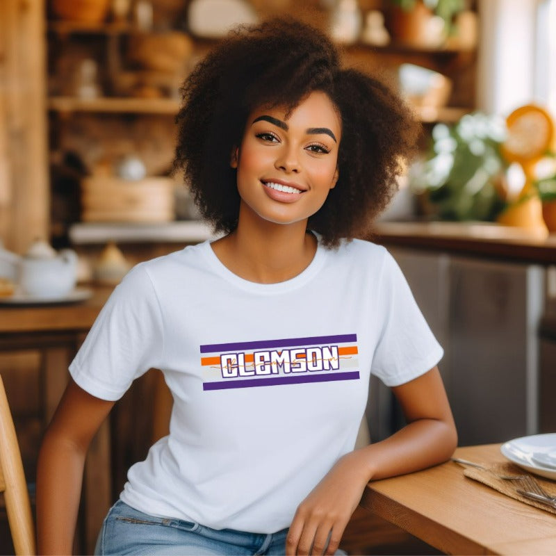 Bella + Canvas 3001 unisex shirt with Clemson University stripe design in purple, orange, and white, with "Clemson" written in bold letters on a white graphic tee.