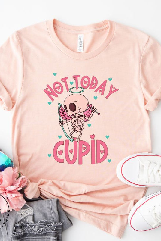 Unleash your rebellious spirit this Valentine's Day with our edgy shirt featuring a skeleton Cupid. The bold "Not Today Cupid" message adds a touch of attitude, making this tee a standout choice for those who march to the beat of their own drum on a peach shirt. 