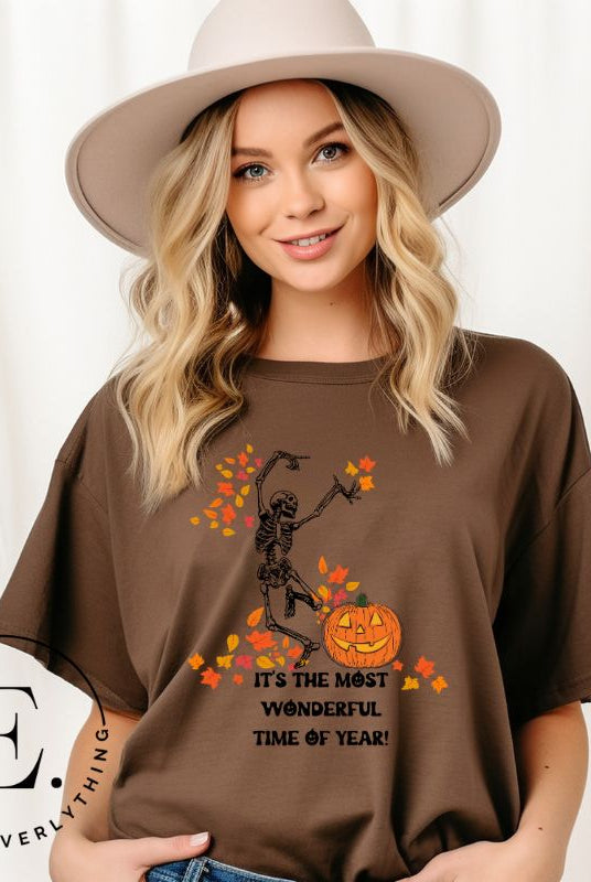Get into the spirit of fall with our Dancing Skeleton T-shirt. This playful shirt features a whimsical skeleton surrounded by falling leaves, on a brown shirt. 