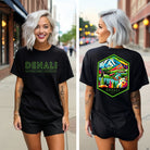 Black Bella + Canvas 3001 t-shirt with front and back Denali National Park designs. The front features "Denali National Park | Alaska - 1917" in neon green text, and the back showcases a colorful, detailed illustration of Denali's landscapes and wildlife.