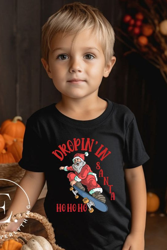 Get your kids in the holiday spirit with our unique, playful tee featuring Santa shredding on a skateboard with the phrase "Dropin' In Santa Ho Ho Ho." On a black shirt. 