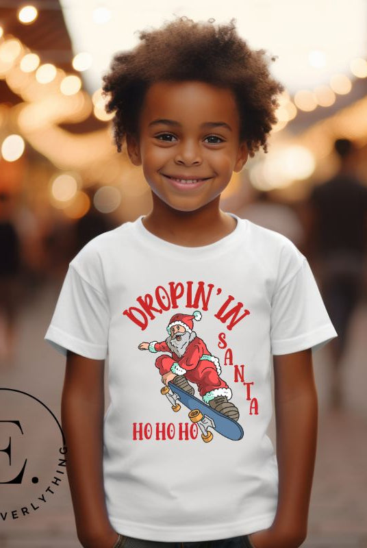 Get your kids in the holiday spirit with our unique, playful tee featuring Santa shredding on a skateboard with the phrase "Dropin' In Santa Ho Ho Ho." On an white shirt. 