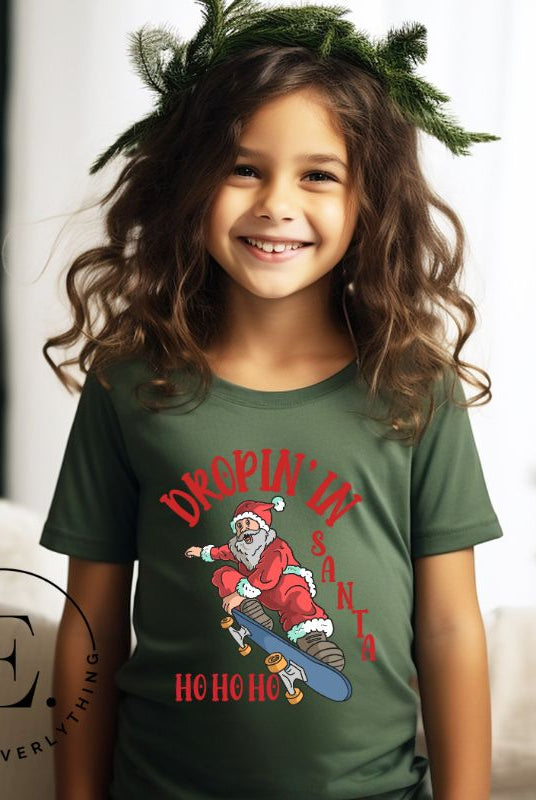Get your kids in the holiday spirit with our unique, playful tee featuring Santa shredding on a skateboard with the phrase "Dropin' In Santa Ho Ho Ho." On a green shirt. 
