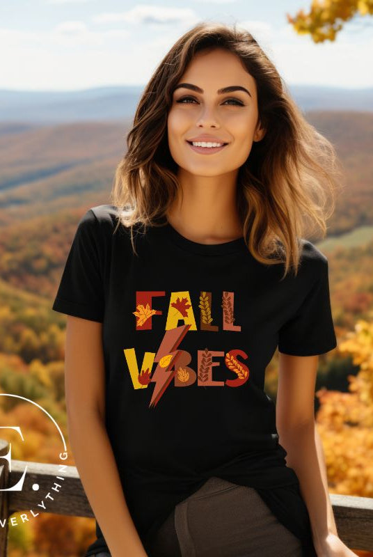 Get into the autumn spirit with our Fall Vibes shirt. Featuring the words 'Fall Vibes' with a creative twist- a lighting bolt replacing the 'I'- this shirt captures the energy of the season. Adorned with leaves, it adds a touch of nature's beauty on a black shirt. 