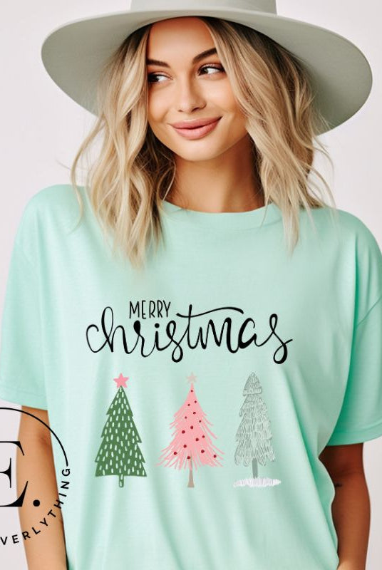 Elevate your festive wardrobe with our trendy shirt and make a chic statement this Christmas. The design features a stylish "Merry Christmas" message along with modern pink and teal Christmas trees, adding a fresh twist to the holiday season on a mint shirt.