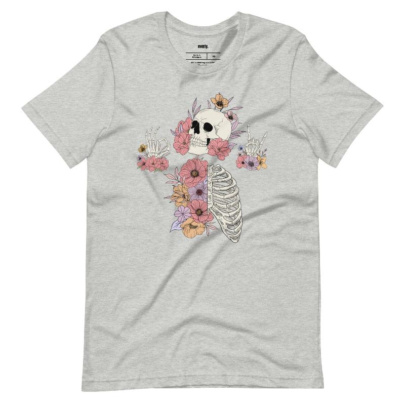 Grey t-shirt featuring a detailed skeleton design with ribcage and hands intertwined with soft, colorful flowers, blending gothic and floral aesthetics.