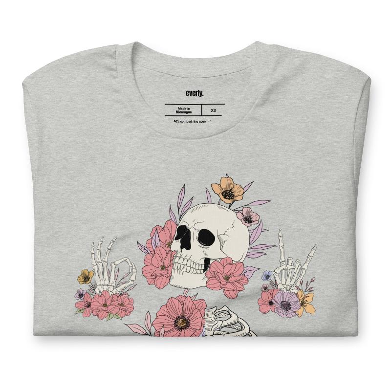 Grey t-shirt featuring a detailed skeleton design with ribcage and hands intertwined with soft, colorful flowers, blending gothic and floral aesthetics.