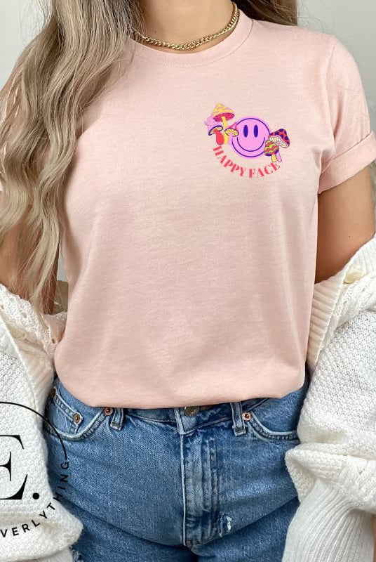 Spread positivity with our delightful t-shirt. The design features a happy face with mushrooms on the side and the words 'Happy Face' on the front pocket on a peach shirt. 