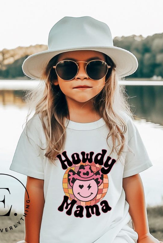 Yeehaw! Get ready to ride into style with our kids' shirt featuring a checkered ball with a winking smiley face, a lightning bolt, and a cowboy hat. With the playful saying 'Howdy Mama,' it's a fun and expressive choice on a white shirt. 
