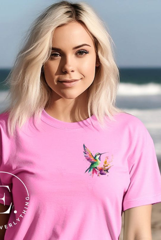 Elevate your style with our stunning t-shirt featuring a watercolor hummingbird delicately placed on the pocket on a pink shirt. 