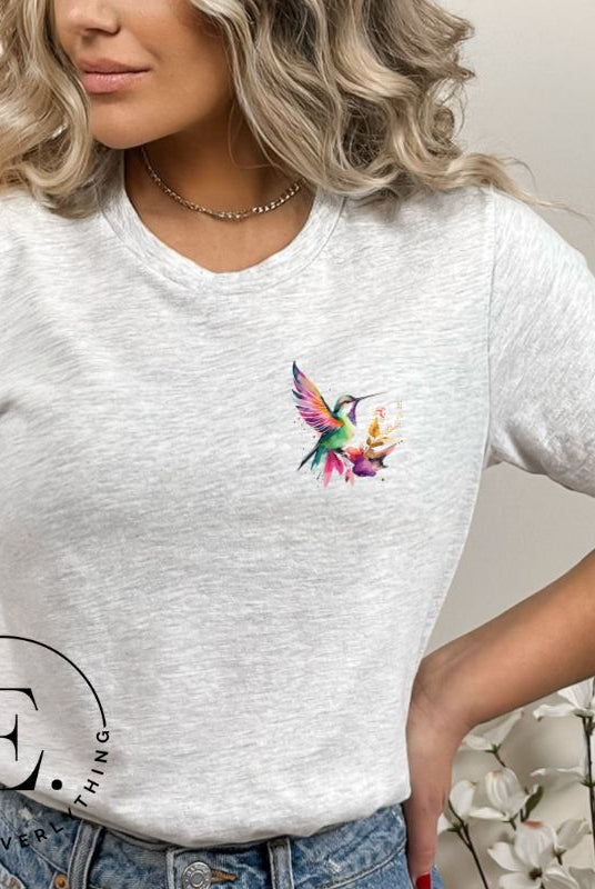 Elevate your style with our stunning t-shirt featuring a watercolor hummingbird delicately placed on the pocket on a grey shirt. 