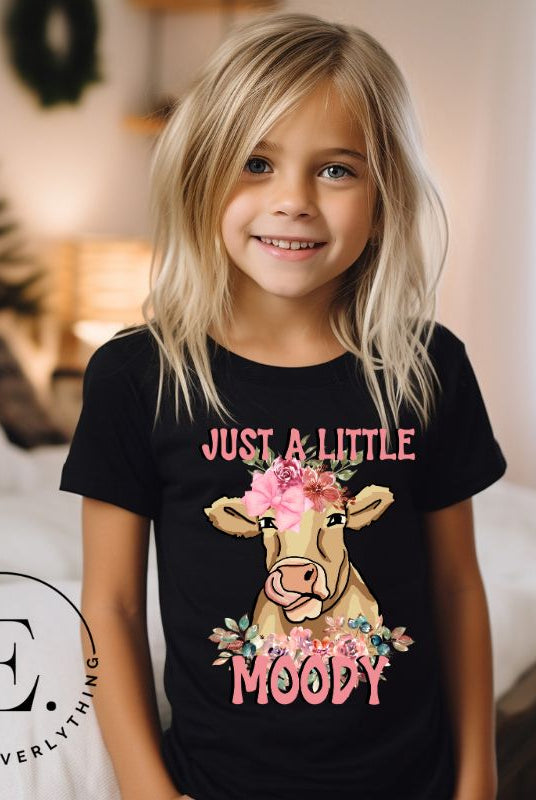Our kid's shirt features an adorable highland cow with flowers and the quote 'Just a Little Moody,' adding humor and personality to the design on a black shirt. 