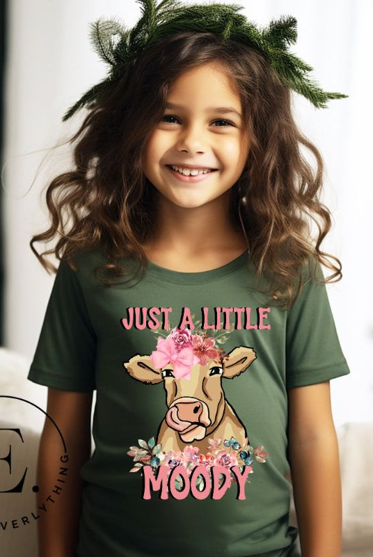 Our kid's shirt features an adorable highland cow with flowers and the quote 'Just a Little Moody,' adding humor and personality to the design on a green shirt. 