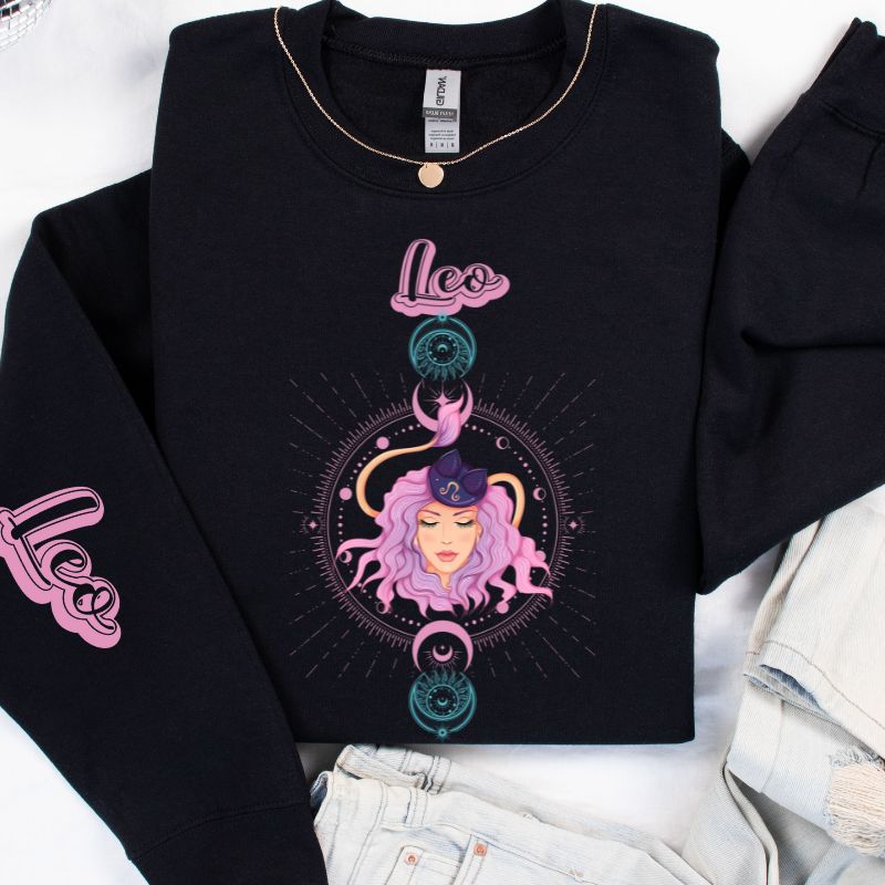 Gildan crewneck pullover sweatshirt featuring a pastel illustration of a Leo figure with flowing purple hair, surrounded by celestial elements. The word "Leo" is written in pink on the sleeve, adding a stylish touch on a black sweatshirt.