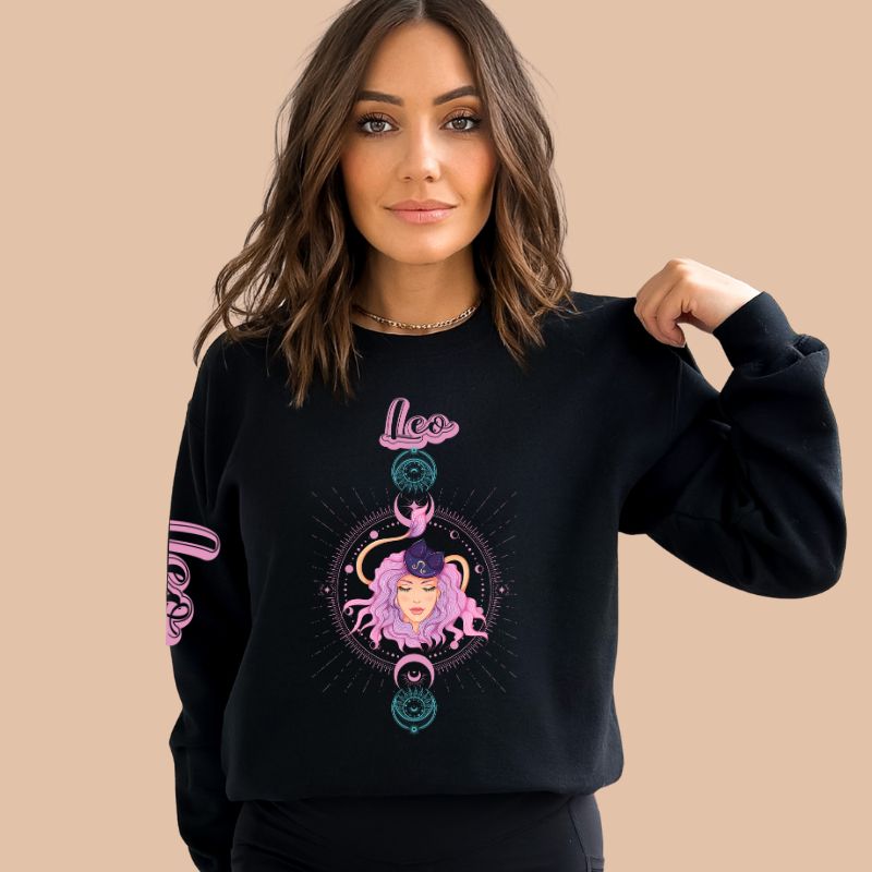 Gildan crewneck pullover sweatshirt featuring a pastel illustration of a Leo figure with flowing purple hair, surrounded by celestial elements. The word "Leo" is written in pink on the sleeve, adding a stylish touch on a black sweatshirt.