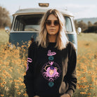 Gildan crewneck pullover sweatshirt featuring a pastel illustration of a Leo figure with flowing purple hair, surrounded by celestial elements. The word "Leo" is written in pink on the sleeve, adding a stylish touch on a black sweatshirt.