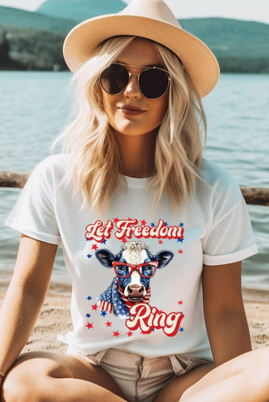 Graphic of a cow wearing sunglasses and a USA-themed scarf, with the text 'Let Freedom Ring' on the front of a white graphic tee.