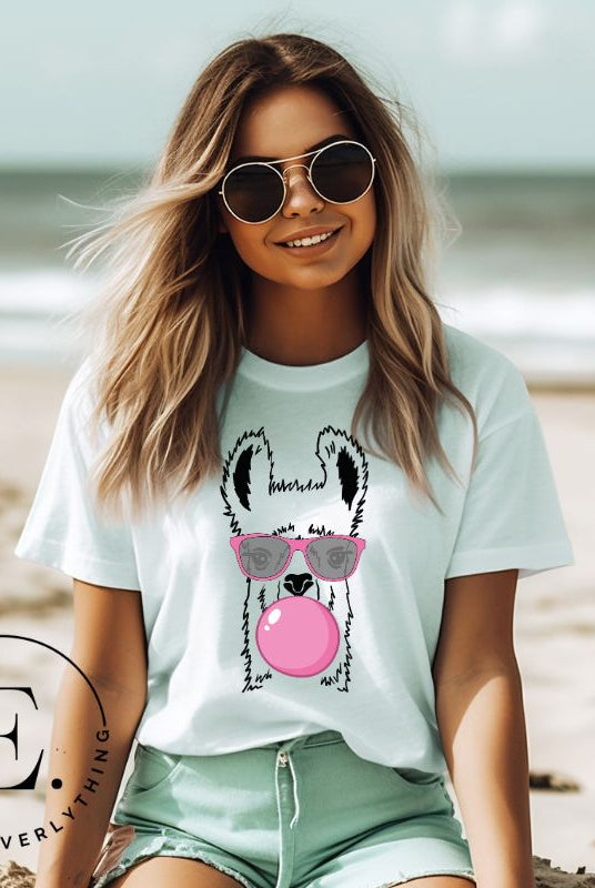 Llama wearing pink sunglasses blowing a bubble gum bubble on a mint colored shirt.