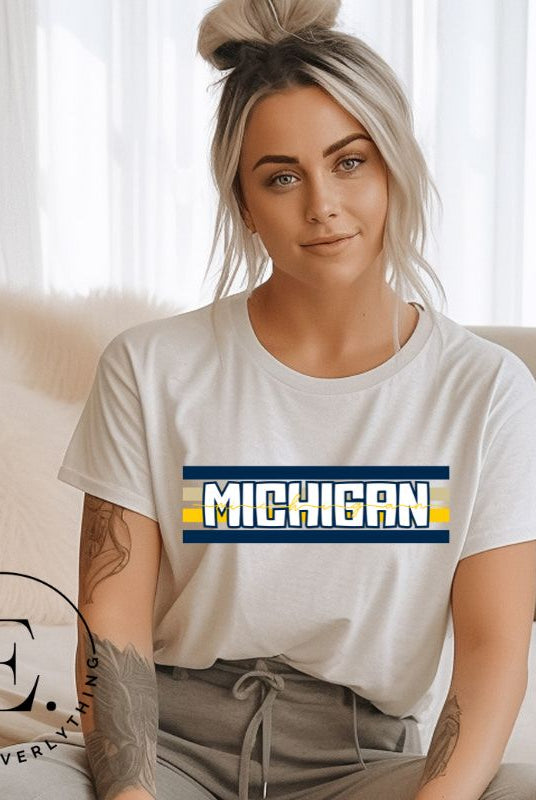 Elevate your collegiate style with our Michigan University graphic tee featuring iconic school colors and bold chest stripes. Emblazoned with "Michigan" in striking lettering, on a soft cream shirt. 