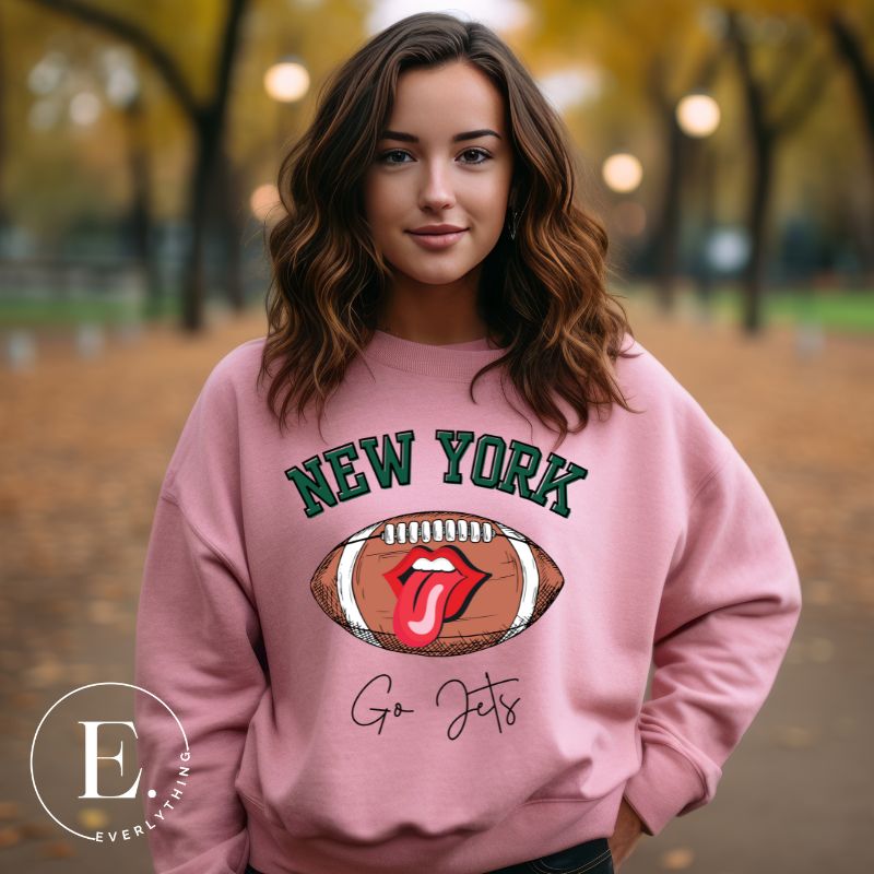 Gear up for game day with this New York Jets sweatshirt, featuring a football and playful lips and tongue design. Emblazoned with the team's rallying cry "Go Jets" and the iconic wordmark New York, on a pink sweatshirt. 