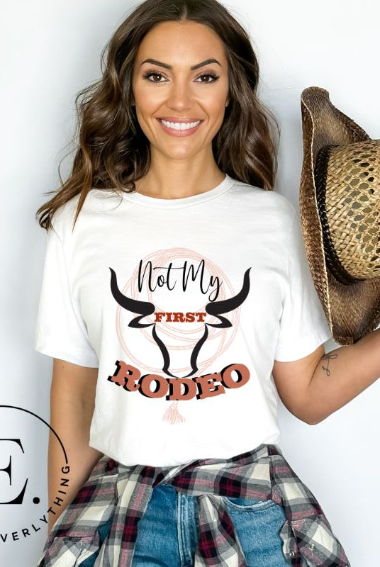 Unleash your cowboy spirit with our country western t-shirt boasting the statement "Not my First Rodeo" alongside bold bull horns and a lasso design on a white shirt. 