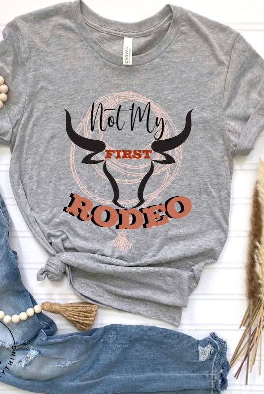 Unleash your cowboy spirit with our country western t-shirt boasting the statement "Not my First Rodeo" alongside bold bull horns and a lasso design on a grey shirt. 
