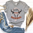 Unleash your cowboy spirit with our country western t-shirt boasting the statement "Not my First Rodeo" alongside bold bull horns and a lasso design on a grey shirt. 