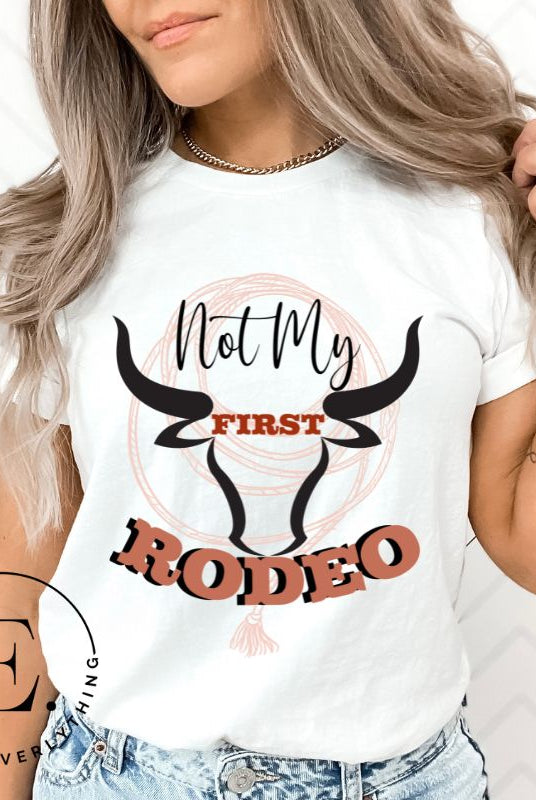 Unleash your cowboy spirit with our country western t-shirt boasting the statement "Not my First Rodeo" alongside bold bull horns and a lasso design on a white shirt. 
