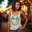 Next Level women's racerback tank top in heather white featuring a vibrant summer design with two palm trees forming an arch over a wave and sunset graphic, showcasing a relaxed and beachy vibe